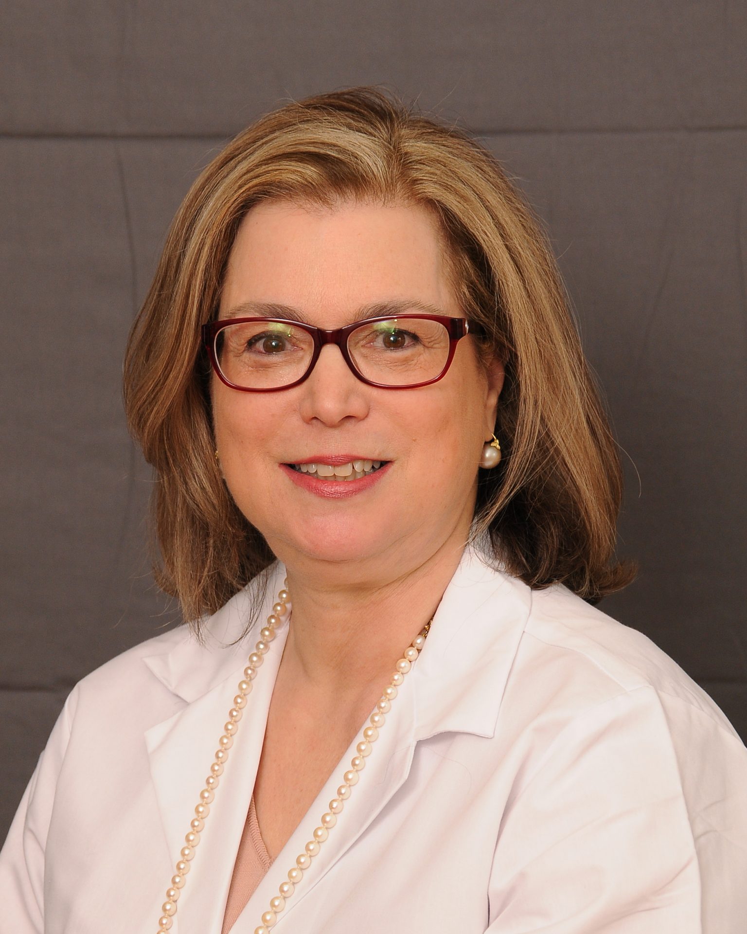 Female dermatologist with glasses, wearing a white coat.